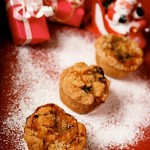 Mini Almond Crumble Mince Pies: on a red background with dusting of icing sugar like snow. In soft focus are dinky presents and a santa ornament.