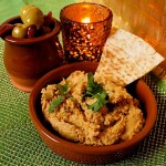 Sweet Potato Hummus with Lime - Easy Dip Recipe. Served in a terracotta tapas dish with fresh coriander garnish and triangle of toasted pitta bread. A dish of olives and a small candle are in the background.