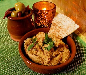 Sweet Potato Hummus with Lime - Easy Dip Recipe. Served in a terracotta tapas dish with fresh coriander garnish and triangle of toasted pitta bread. A dish of olives and a small candle are in the background.