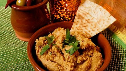 Sweet Potato Hummus with Lime - Easy Dip Recipe. Served in a terracotta tapas dish with fresh coriander garnish and triangle of toasted pitta bread. A dish of olives and a small candle are in the background.