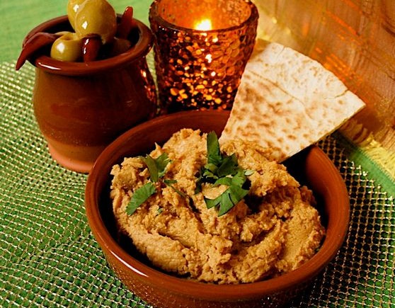 Sweet Potato Hummus with Lime - Easy Dip Recipe. Served in a terracotta tapas dish with fresh coriander garnish and triangle of toasted pitta bread. A dish of olives and a small candle are in the background.