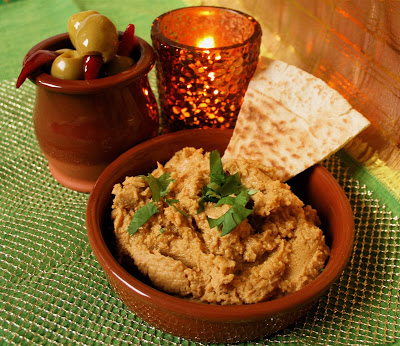 Sweet Potato Hummus with Lime - Easy Dip Recipe. Served in a terracotta tapas dish with fresh coriander garnish and triangle of toasted pitta bread. A dish of olives and a small candle are in the background.
