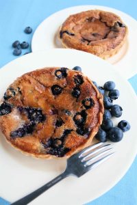Blueberry Cinnamon Tarts: A golden blueberry tart on a white plate with raw blueberries and a fork.