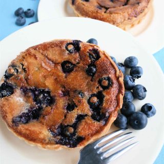 Blueberry Cinnamon Tarts: A golden blueberry tart on a white plate with raw blueberries and a fork.