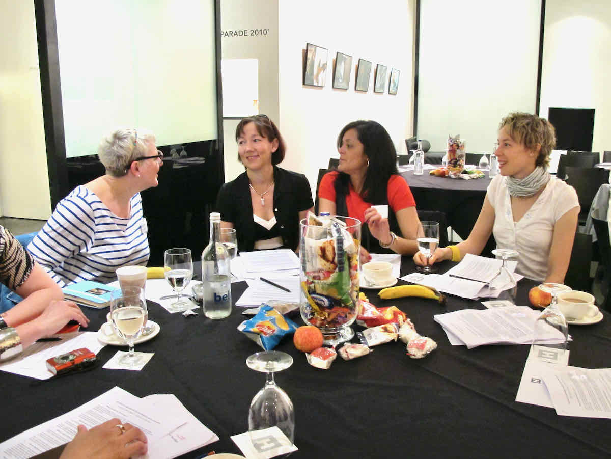 Highlights Food Blogger Connect: Four ladies at a conference table in conversation, there are snacks and drinks on the table and a black tablecloth. The background is white and brightly lit.