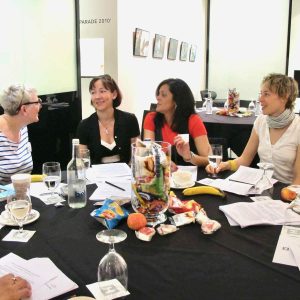 Highlights Food Blogger Connect: Four ladies at a conference table in conversation, there are snacks and drinks on the table and a black tablecloth. The background is white and brightly lit.