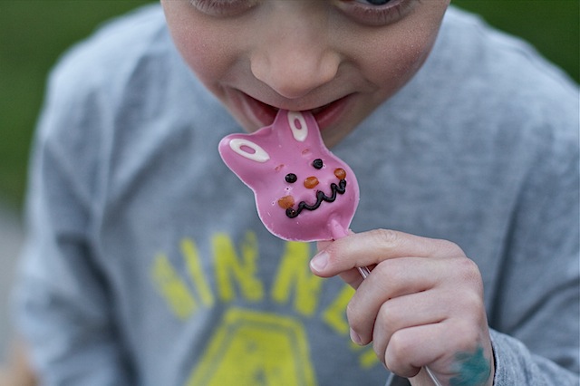 Easter Bunny Pops - a small boy holds a small pink chocolate bunny on a stick in front of his face taking a bite. 