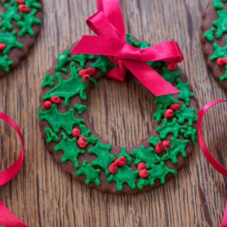 Christmas Wreath Cookie decorated with green holly and red berry icing. A red ribbon bow to decorate or hang them on a Christmas Tree.