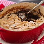 Nutella Semolina Meringue Pudding in an oval shaped red casserole dish, on a red gingham cloth
