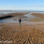 Whitstable beach on a bright winter day facing the sea, the tide is out and a small boy runs towards the camera.