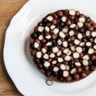 Chocolate Quark Cheesecake - Easy No Bake Recipe. Seen from above, chocolate cheesecake wtih crunchy biscuit pieces. A slice has been cut away and sites on a stripey blue plate with a fork. A bag of McVities Nibbles to the side.