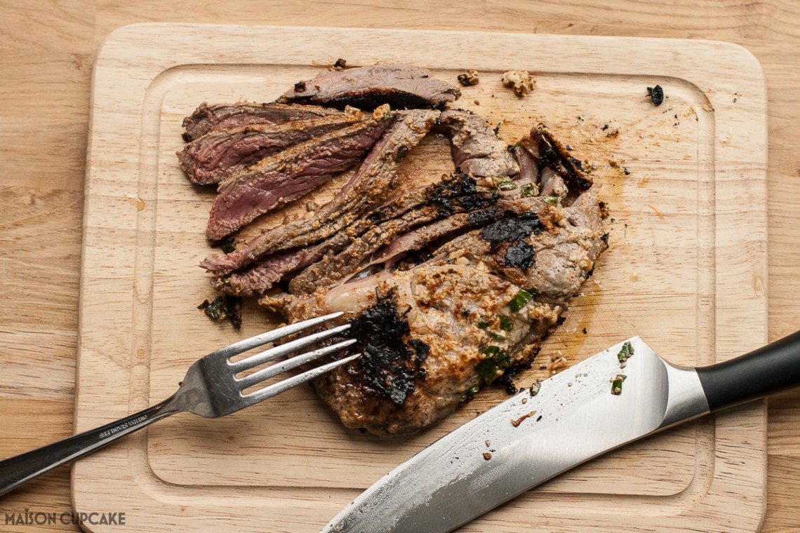 Roast lamb meat in slices on a wooden chopping board alongside a fork and chef's knife.