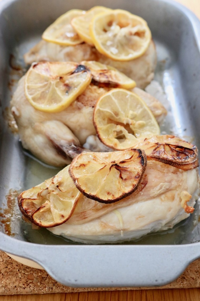 Microwave chicken supreme recipe. Three cooked chicken pieces with lemon slices in a metal oven dish - portrait layout