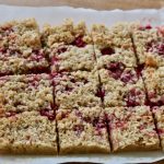 Raspberry flapjacks with coconut traybake, homemade and sliced into a dozen squares on baking paper. Fresh raspberry fruit is visible and has stained the paper.