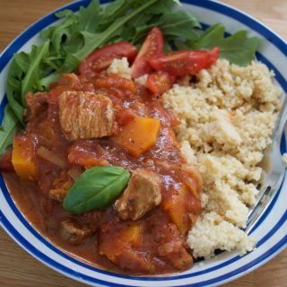Turkey Thigh Tagine stew served in a blue stripey bowl alongside rocket and cous cous - landscape