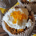 Carrot cake muffins topped with white cream cheese icing and grated carrot.