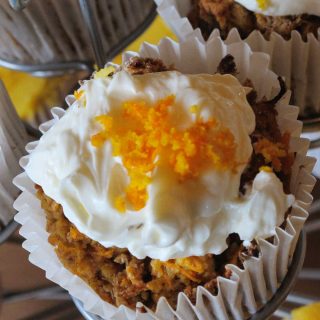 Carrot cake muffins topped with white cream cheese icing and grated carrot.