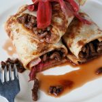 Spicy pork pancakes with rhubarb served in rolls with drizzle of sauce and extra cooked pink rhubarb on top.